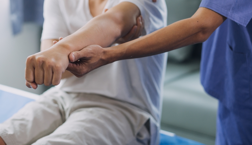 Physiotherapist working examining treating injured arm of athlete male patient